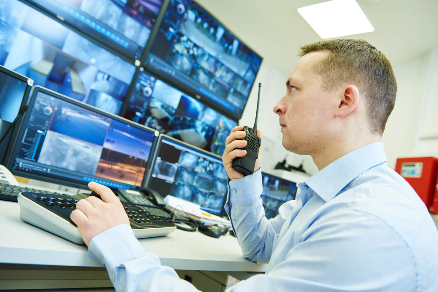 A man talking into a hand held radio infront of monitors .