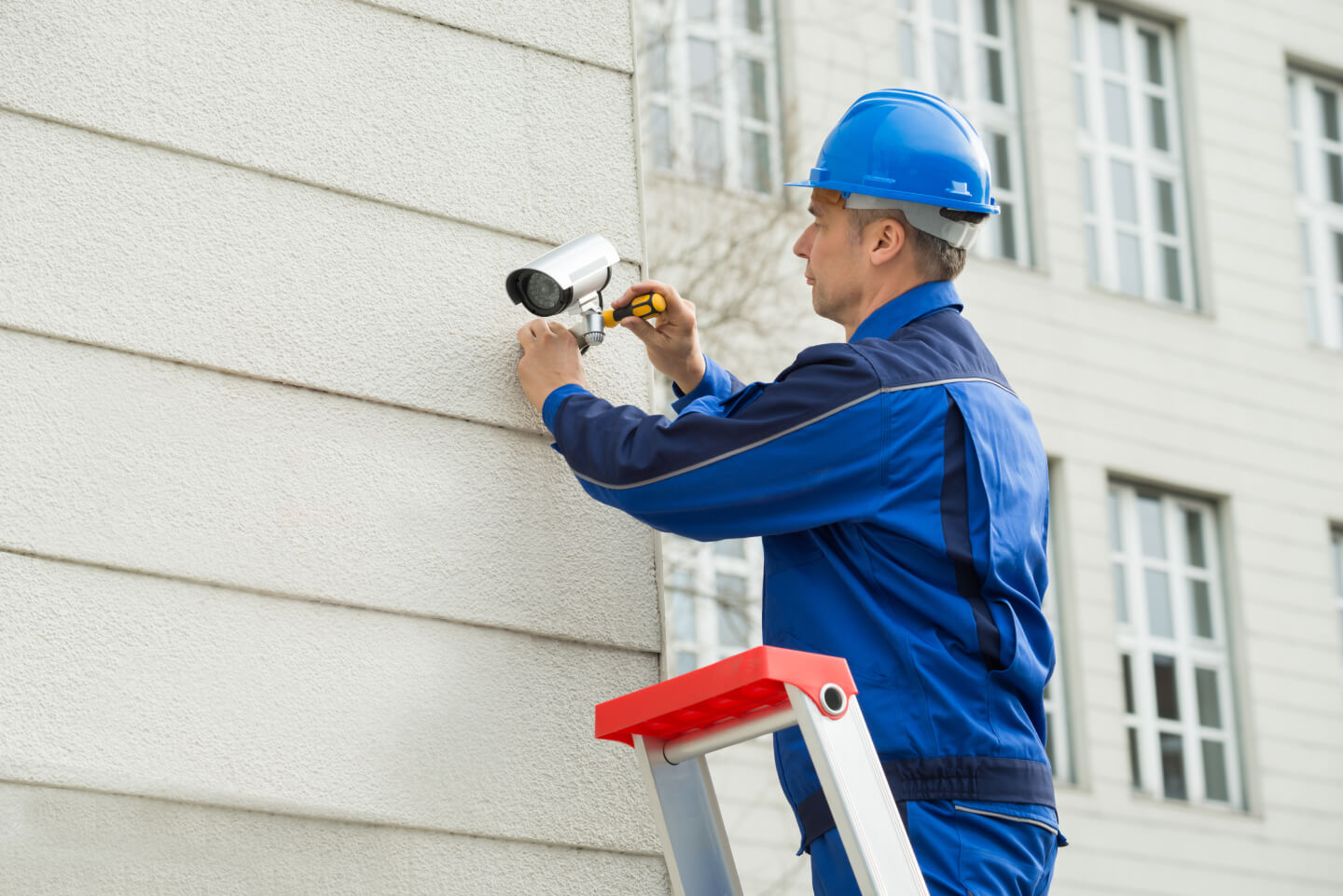 A man installing a CCTV camera outside a building .